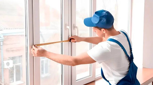 Handwerker misst ein weißes Kunststofffenster mit einem Maßband